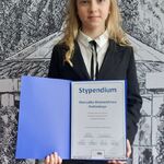 Dziewczynka w eleganckim czarnym garniturze trzyma otwartą teczkę z dyplomem Stypendium Marszałka Województwa Podlaskiego