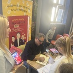 mężczyzna siedzący przy stole w otoczeniu czytelników składający podpis w książce